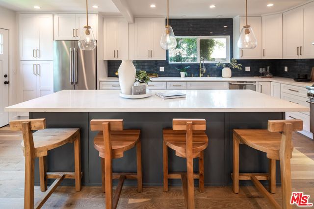 a kitchen with stainless steel appliances granite countertop a table chairs refrigerator and sink