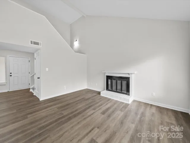 an empty room with wooden floor fireplace and windows