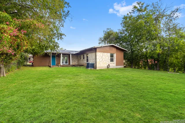 a view of a yard in front of a house with plants and large tree
