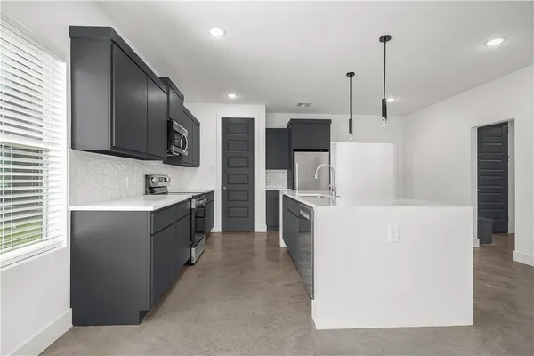 a large kitchen with a large counter top a sink stainless steel appliances and cabinets