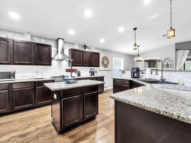 a large kitchen with stainless steel appliances kitchen island granite countertop a sink a stove and a wooden floor