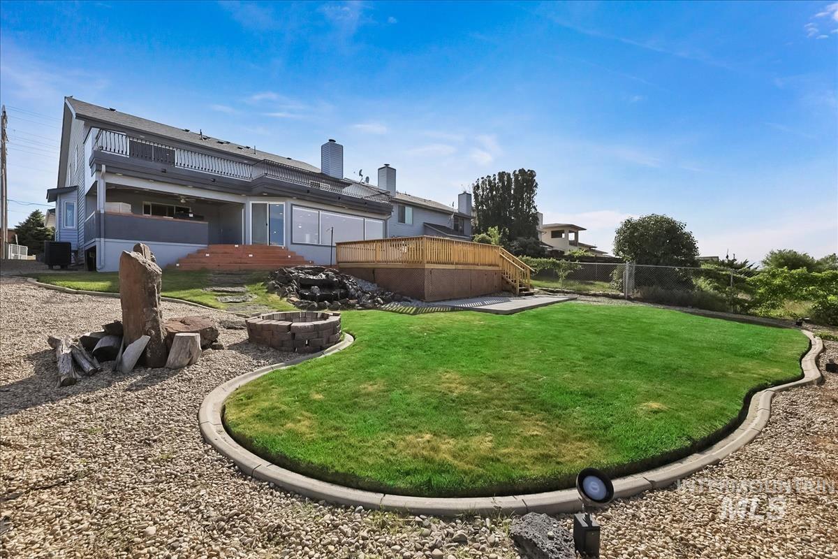 Expansive backyard featuring a manicured lawn, a gravel patio, a stone fire pit, and a tiered water feature