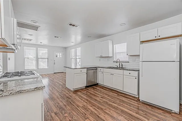 a kitchen with granite countertop a refrigerator sink stove and white cabinets