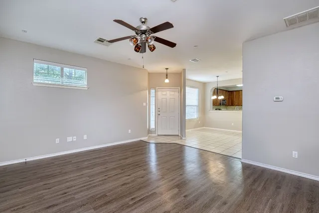 a view of an empty room with wooden floor and a ceiling fan