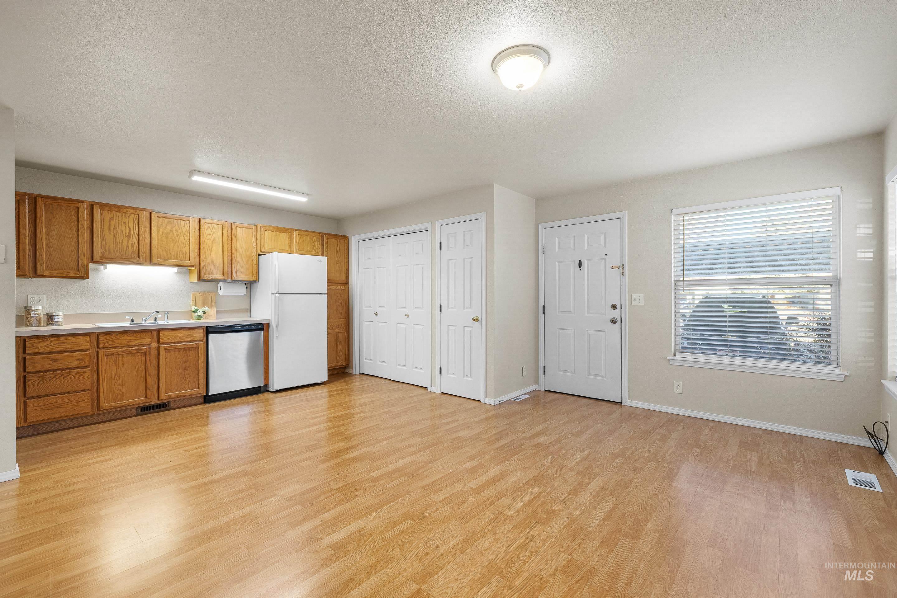8909 West Irving Street, Unit 101 Boise, ID 83704 - Photo 12 of 33 Kitchen featuring light countertops, brown cabinetry, dishwasher, light wood-type flooring, and freestanding refrigerator