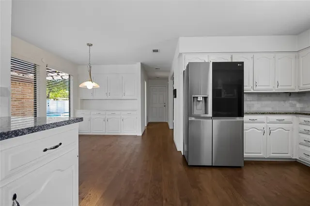 a kitchen with stainless steel appliances granite countertop a refrigerator a sink and white cabinets with wooden floor