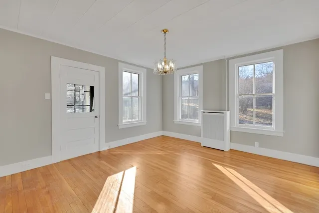 a view of an empty room with window and hardwood floor