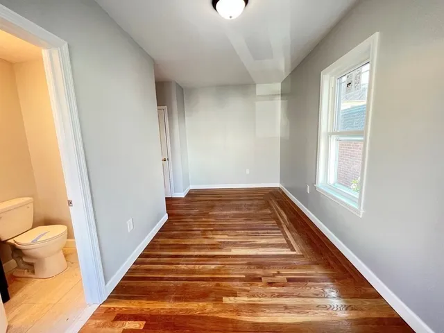a view of a hallway with wooden floor and a toilet