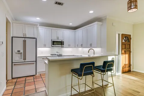 a kitchen with stainless steel appliances granite countertop a refrigerator a sink a stove a dining table and chairs with wooden floor