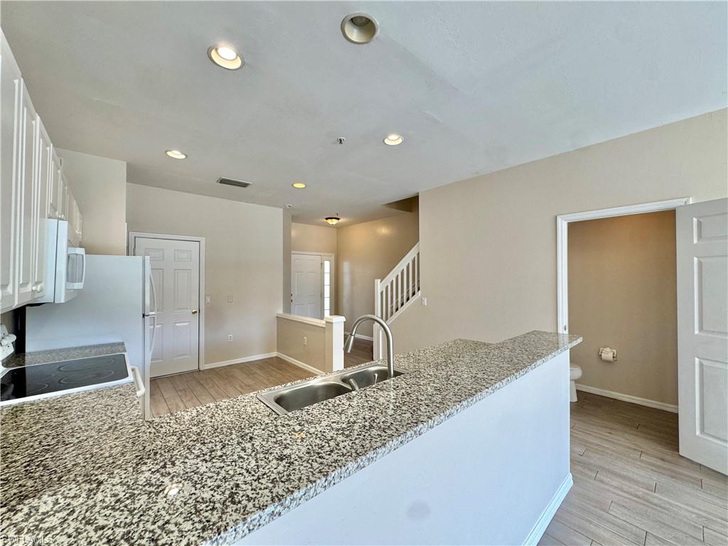 912 Hampton Circle, Unit 92 Naples, FL 34105 - Photo 8 of 31 Kitchen featuring light wood finished floors, a peninsula, electric range, light stone countertops, and white cabinetry