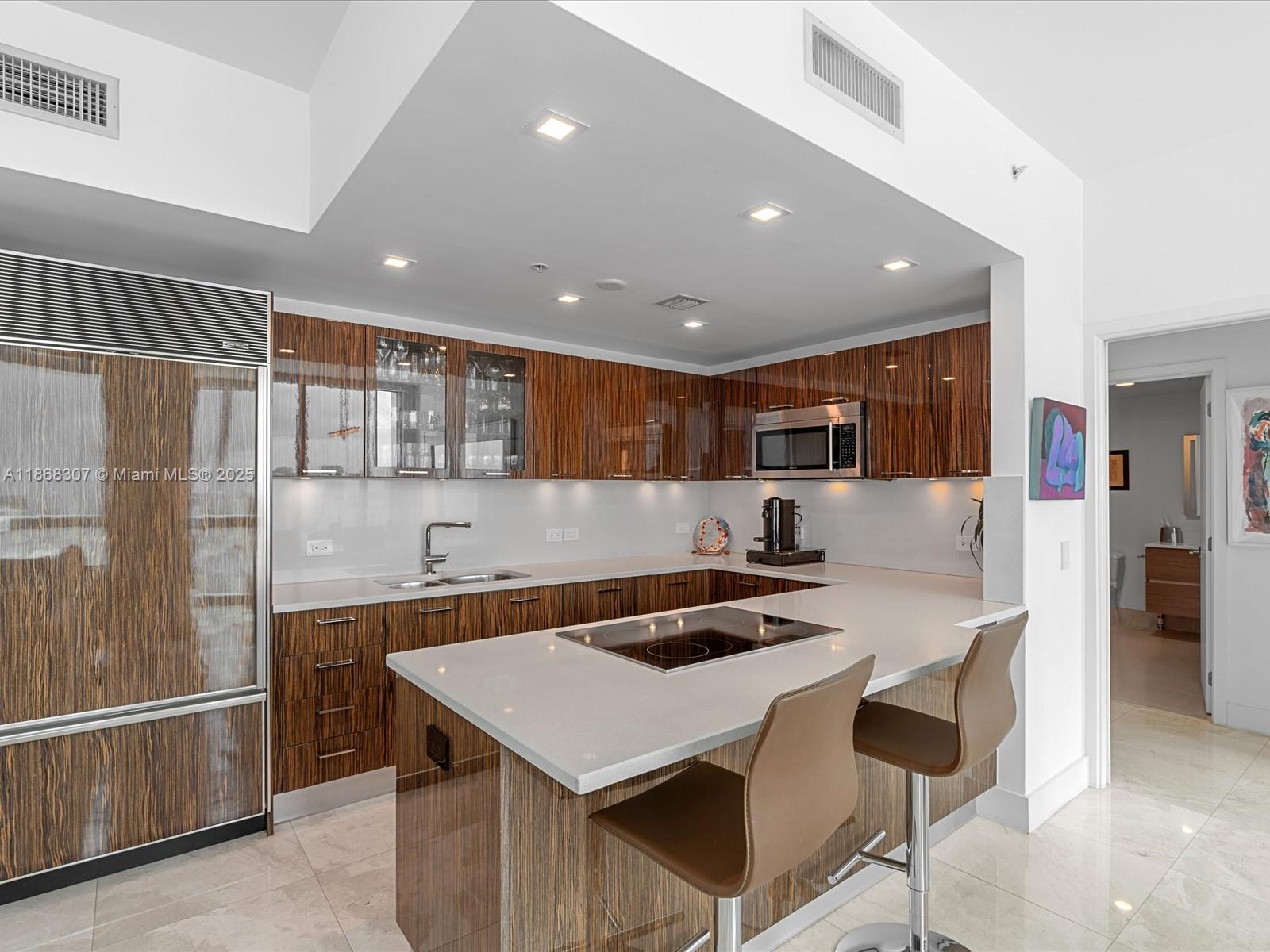 6899 Collins Avenue, Unit 1010 Miami Beach, FL 33141 - Photo 6 of 37 a kitchen with a table chairs refrigerator and cabinets