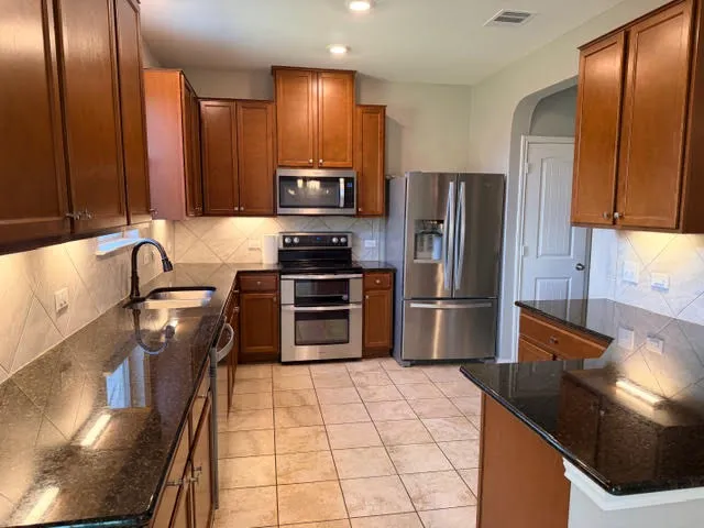 a kitchen with stainless steel appliances granite countertop a refrigerator a stove and a sink with wooden cabinets