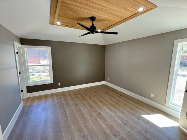 an empty room with wooden floor chandelier fan and windows