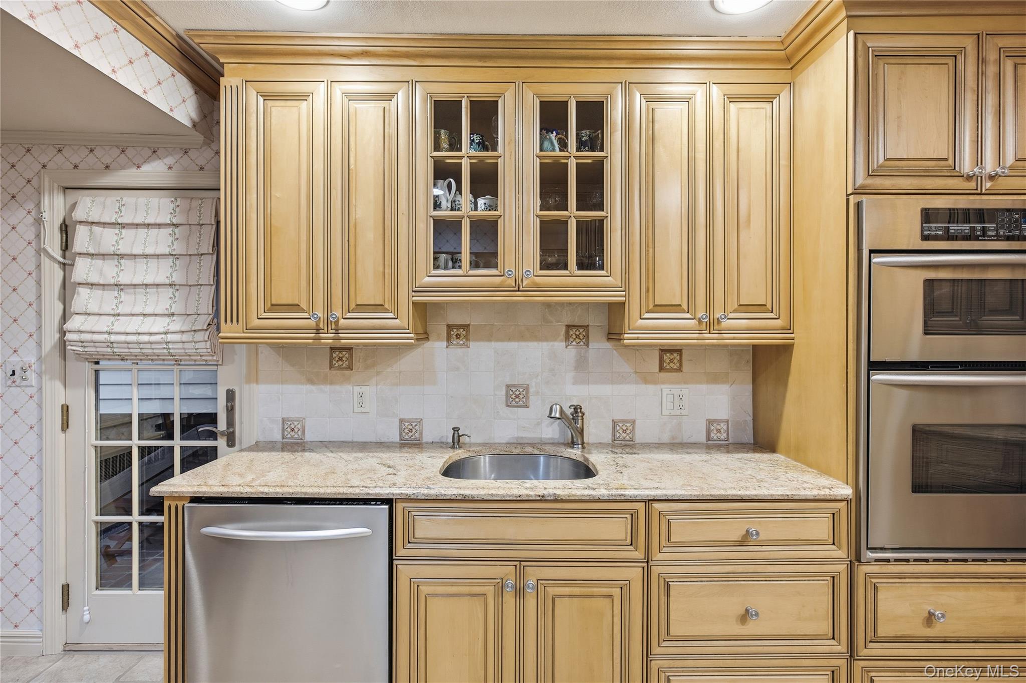 7 Judith Street Plainview, NY 11803 - Photo 17 of 45 Kitchen with stainless steel appliances, glass insert cabinets, light stone countertops, decorative backsplash, and wallpapered walls