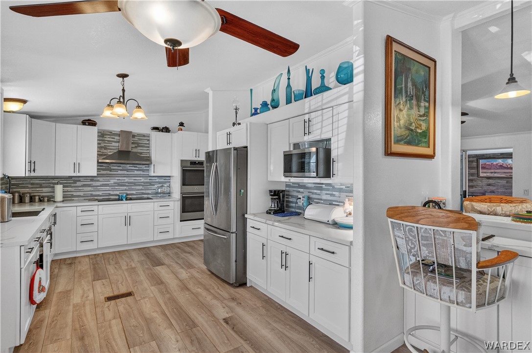 784 Pegasus Ranch Road Bullhead City, AZ 86429 - Photo 11 of 100 Contemporary kitchen featuring wood-finish flooring, white cabinetry, stainless steel appliances, and a mosaic tile backsplash
