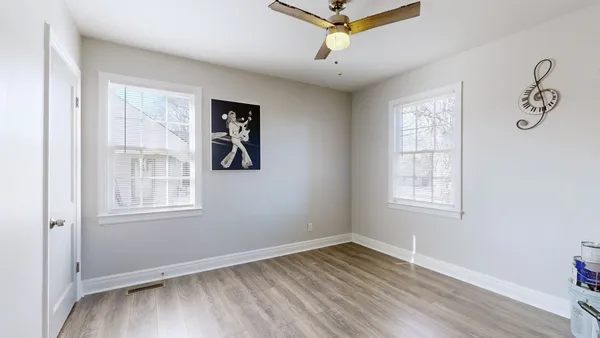 an empty room with wooden floor chandelier fan and windows