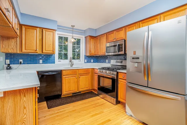 a kitchen with stainless steel appliances granite countertop a refrigerator a sink dishwasher a stove top oven and a dining table with wooden floor