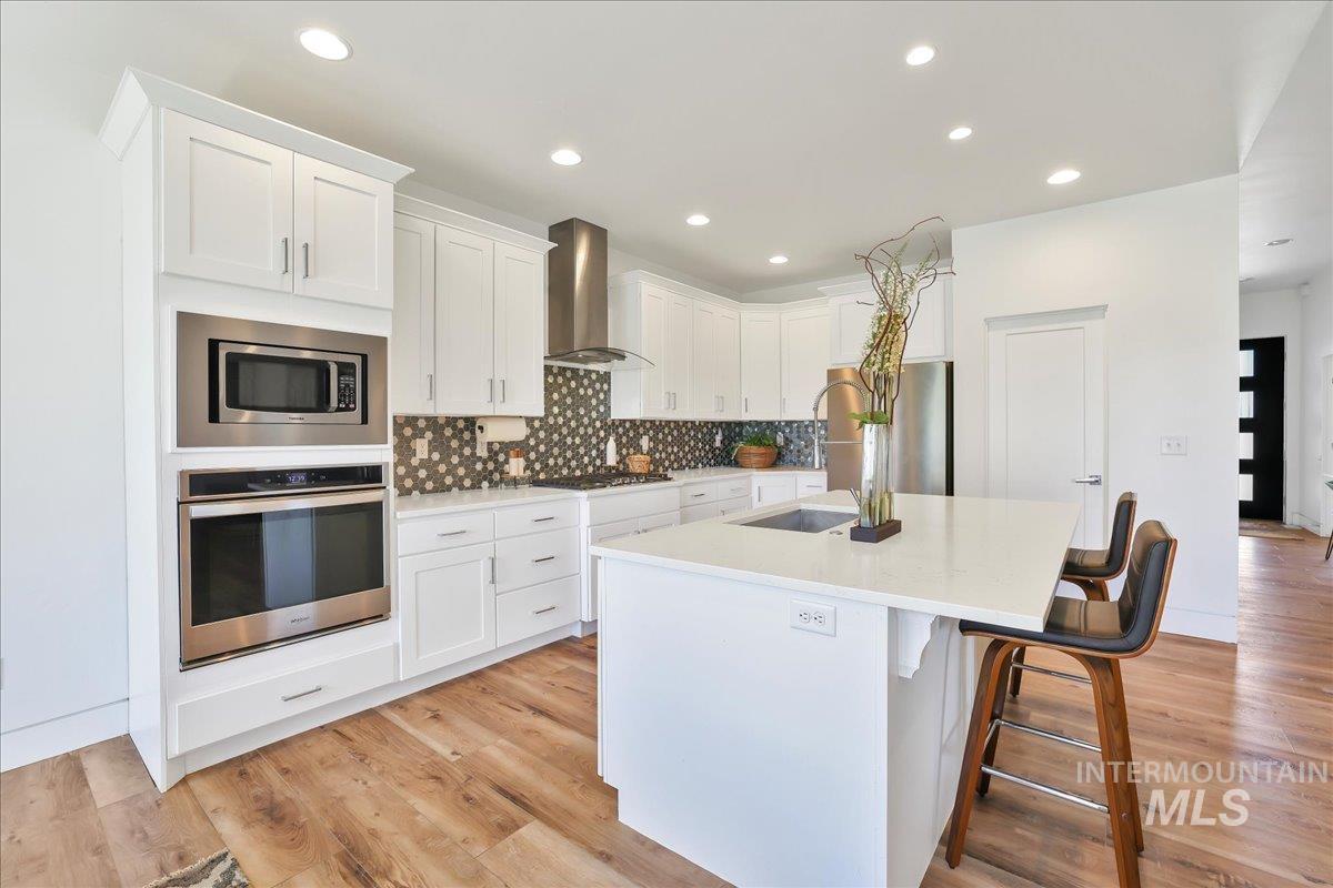 957 Birchton Loop Twin Falls, ID 83301 - Photo 9 of 32 Kitchen with decorative backsplash, stainless steel appliances, light wood-style floors, a kitchen island with sink, and recessed lighting