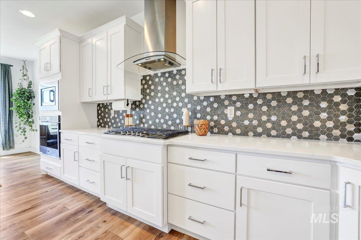 957 Birchton Loop Twin Falls, ID 83301 - Photo 10 of 32 Kitchen with ventilation hood, white cabinets, appliances with stainless steel finishes, tasteful backsplash, and light wood-style flooring