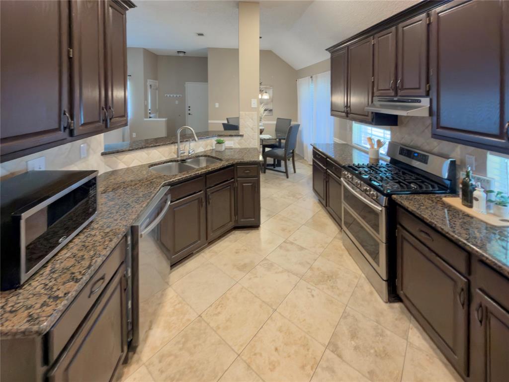 4234 Timberglen Road Dallas, TX 75287 - Photo 9 of 32 Kitchen featuring dark wood cabinetry, granite countertops, stainless steel appliances, and tile flooring