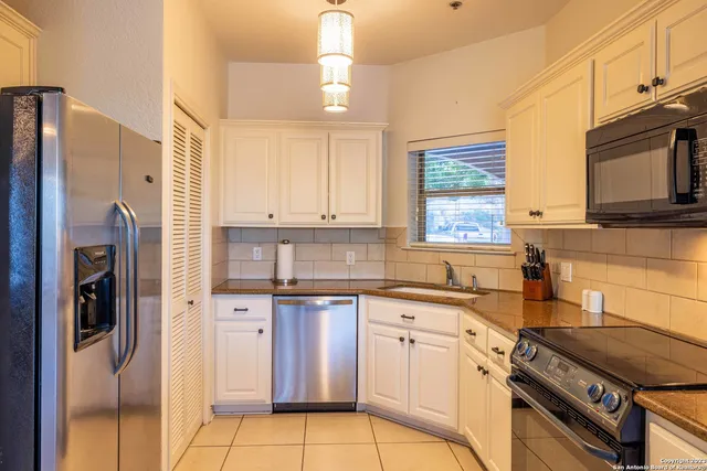 a kitchen with stainless steel appliances granite countertop a refrigerator a sink dishwasher a stove and white cabinets with wooden floor