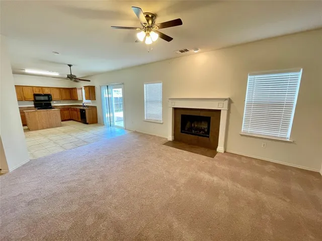 a view of a livingroom with a fireplace a ceiling fan and a kitchen view