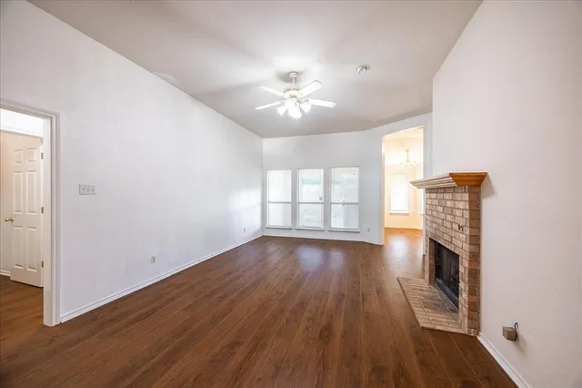 an empty room with wooden floor fireplace and windows