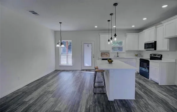 a kitchen with stainless steel appliances granite countertop a refrigerator a stove top oven a sink dishwasher and a dining table with wooden floor