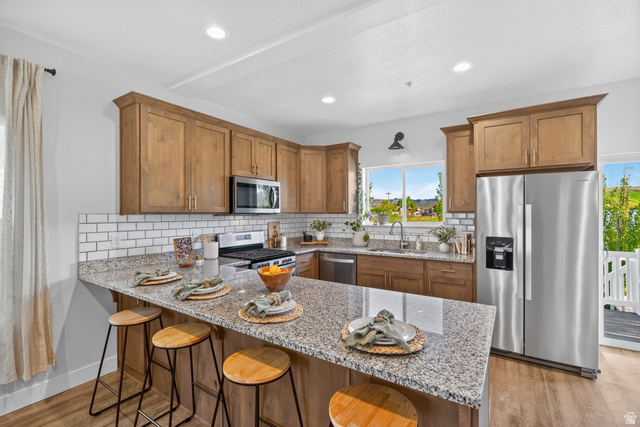 681 Island Road Morgan, UT 84050 - Photo 8 of 49 Kitchen featuring a granite-topped island with seating, wood-finish flooring, stainless steel appliances, and subway tile backsplash