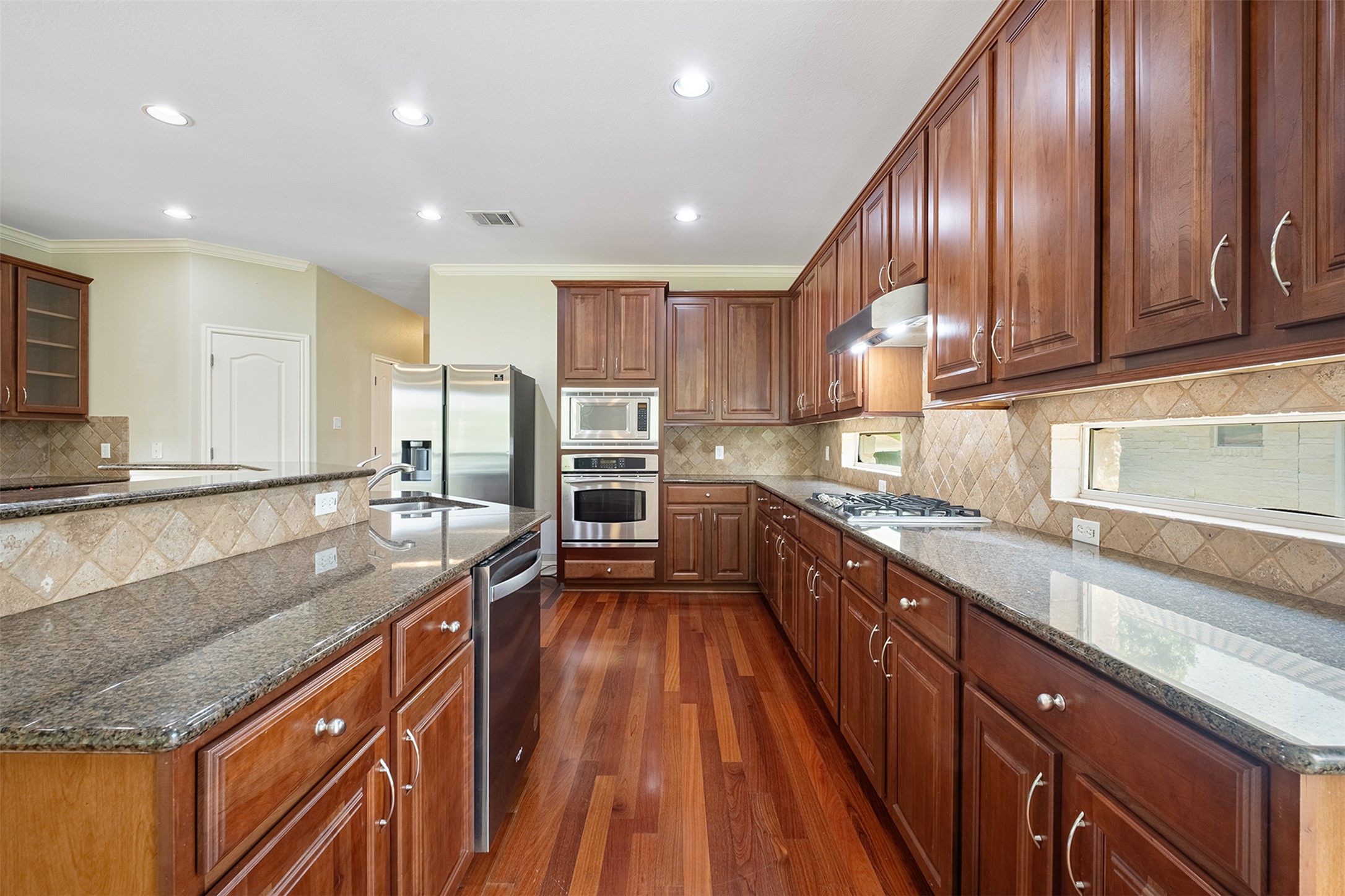 14909 Spillman Ranch Loop Austin, TX 78738 - Photo 14 of 40 Kitchen featuring crown molding, stainless steel appliances, backsplash, under cabinet range hood, and dark wood-type flooring