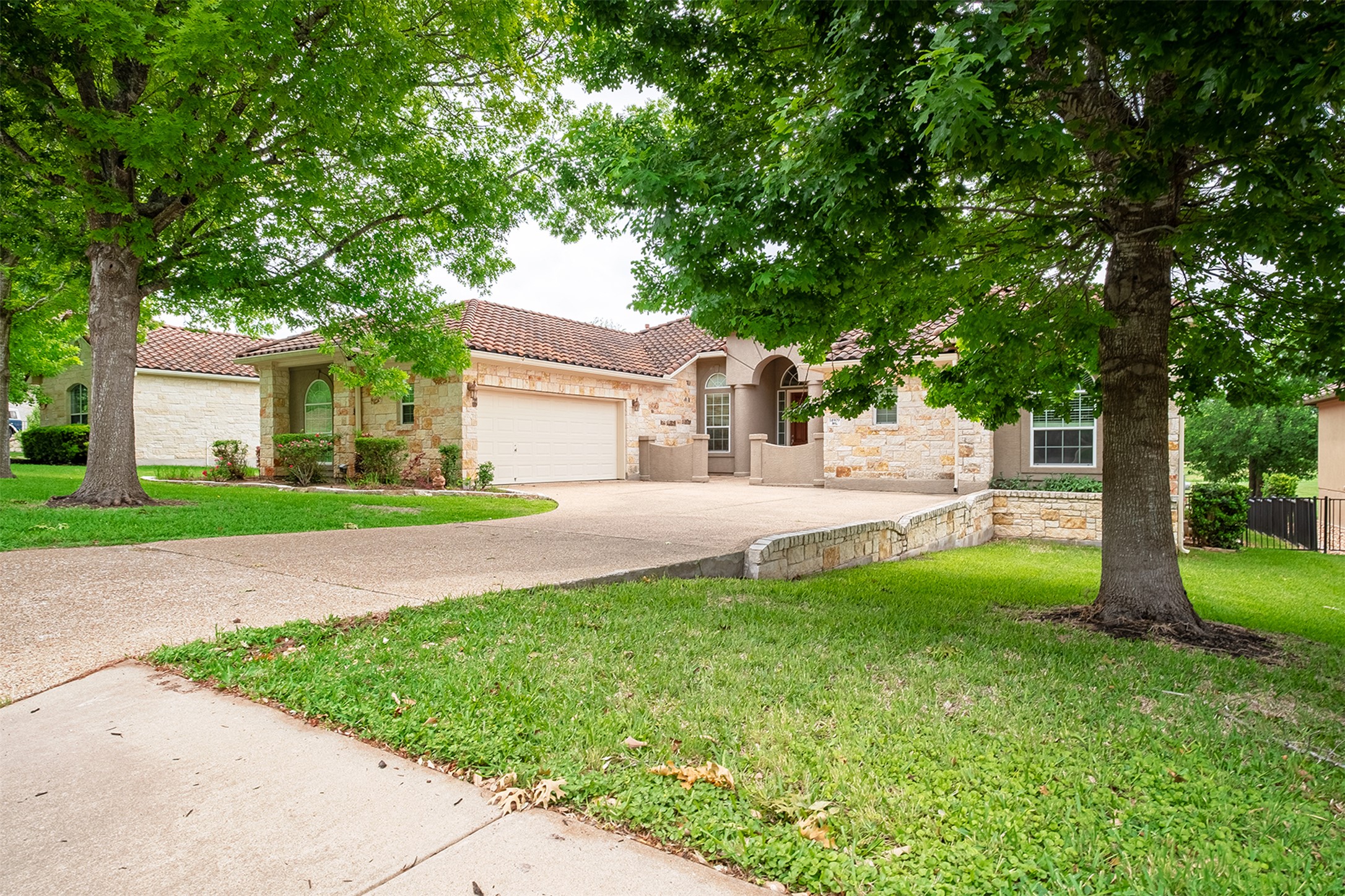 14909 Spillman Ranch Loop Austin, TX 78738 - Photo 3 of 40 View of front facade featuring a tiled roof, a front lawn, driveway, stone siding, and a garage