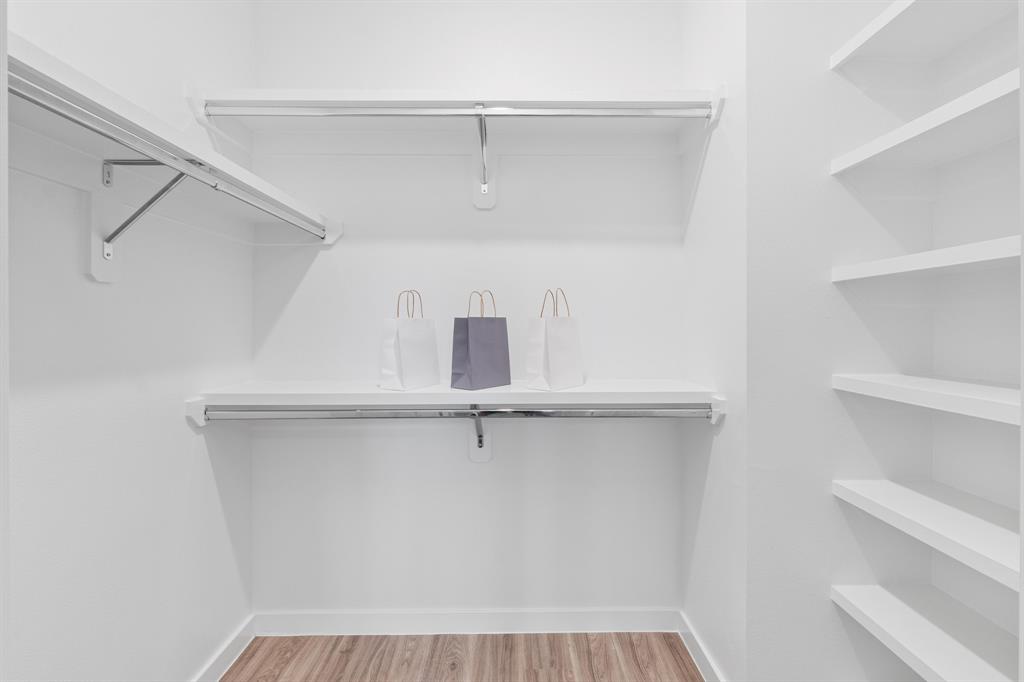 4801 Springdale Road, Unit 2010 Austin, TX 78723 - Photo 22 of 34 Walk-in closet featuring built-in shelving, two hanging rods, white walls, and wood-finish flooring