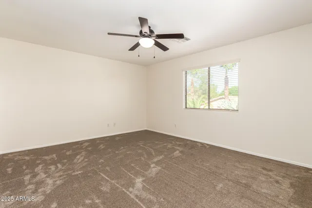 an empty room with ceiling fan and windows