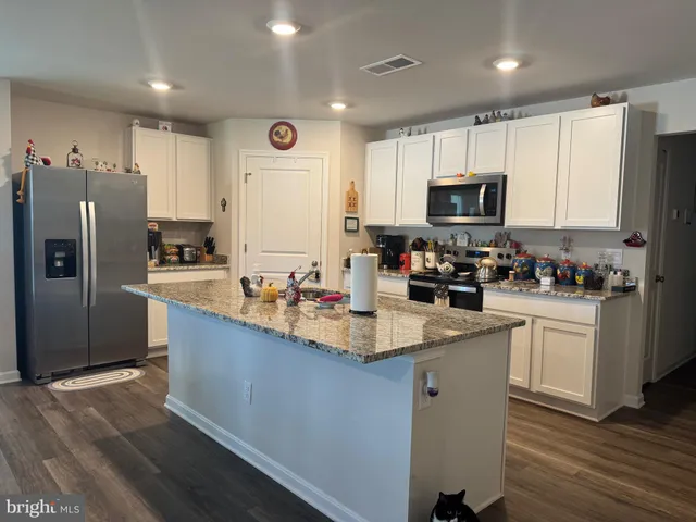 a kitchen with granite countertop a refrigerator a sink a stove a microwave and island with wooden floor