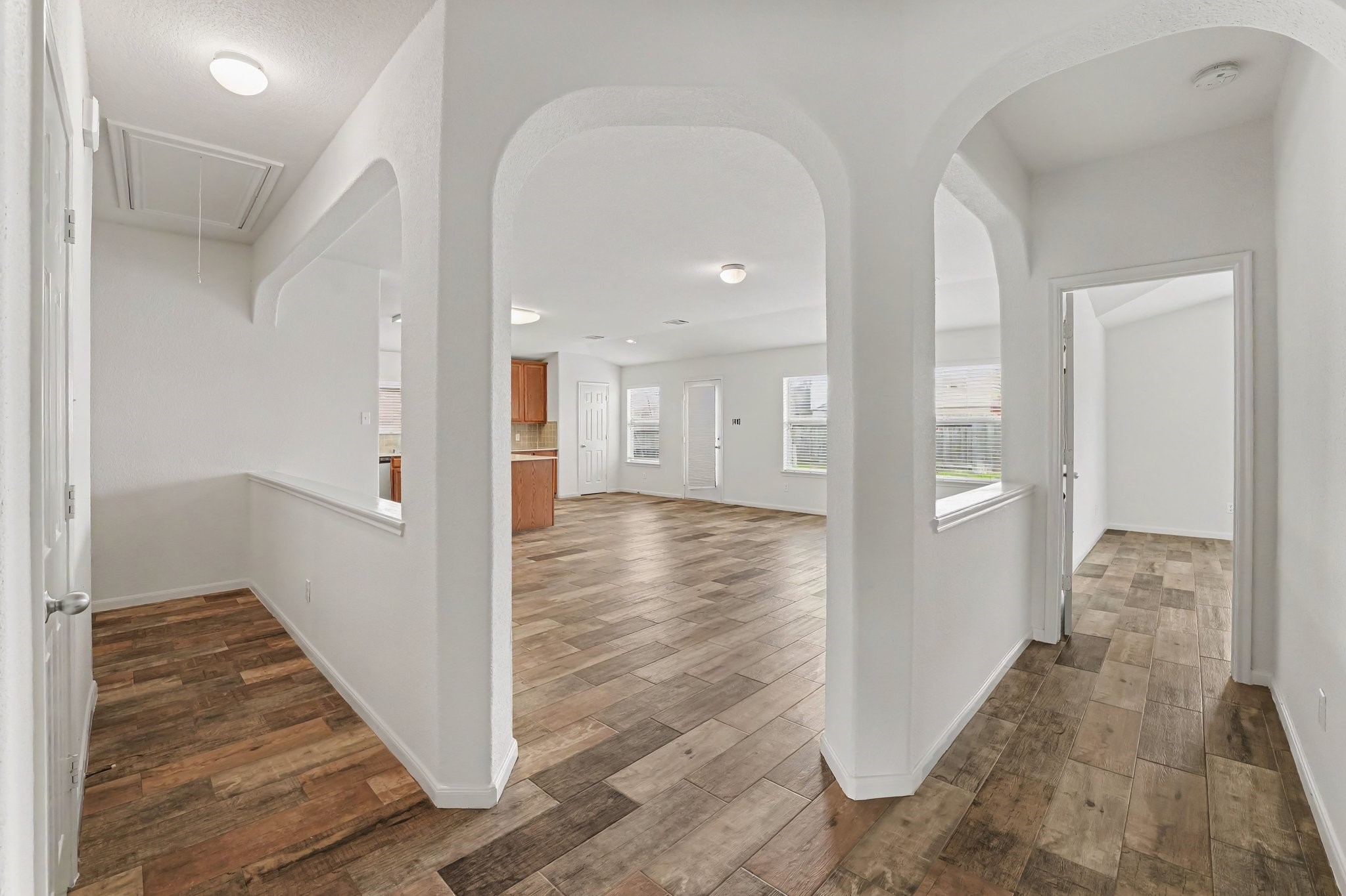 21427 Blooming Rock Lane Spring, TX 77379 - Photo 22 of 32 This photo showcases a bright, open-concept interior featuring wood-look flooring, arched doorways, and ample natural light. The layout includes a spacious area leading to a kitchen with visible cabinetry and a glimpse of a separate room.