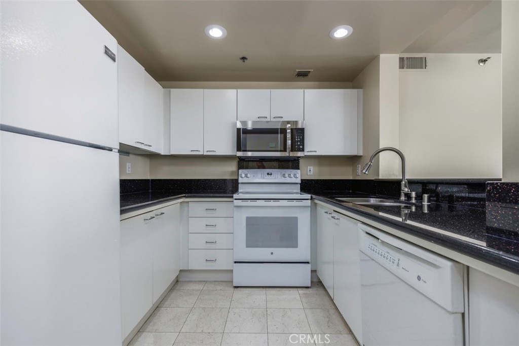 525 East Seaside Way, Unit 704 Long Beach, CA 90802 - Photo 12 of 38 a kitchen with granite countertop white cabinets and stainless steel appliances
