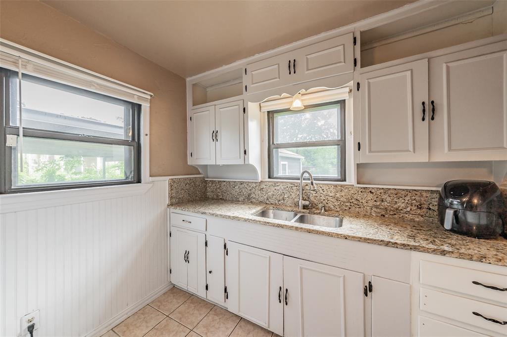1802 Keneipp Road Carrollton, TX 75006 - Photo 15 of 22 The kitchen features white cabinetry with dark hardware, granite-style countertops, a stainless steel double sink, and tiled flooring