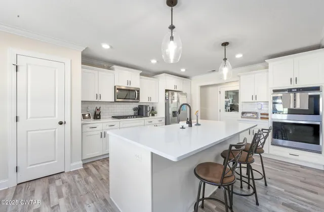 a kitchen with stainless steel appliances kitchen island granite countertop a table chairs refrigerator and microwave