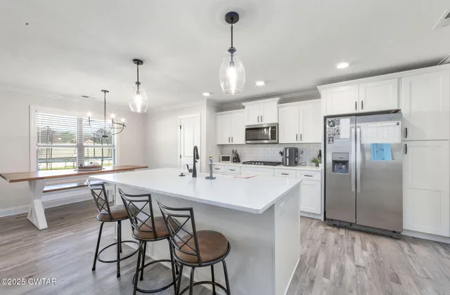 a kitchen with stainless steel appliances a dining table chairs stove refrigerator and cabinets