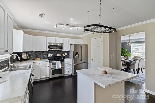 a kitchen with stainless steel appliances a stove a sink dishwasher a refrigerator and white cabinets with wooden floor