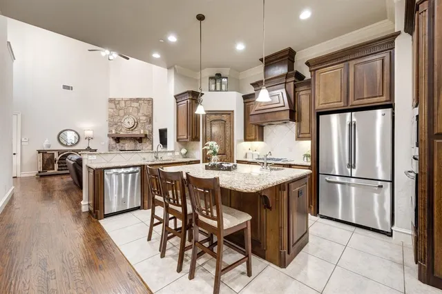 a kitchen with stainless steel appliances granite countertop a kitchen island a stove a refrigerator a sink a dining table and chairs with wooden floor