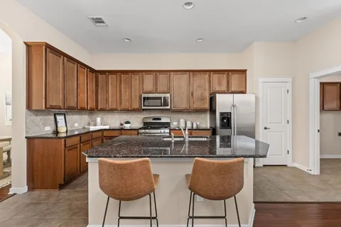 a kitchen with stainless steel appliances granite countertop a stove a sink a refrigerator a dining table and chairs