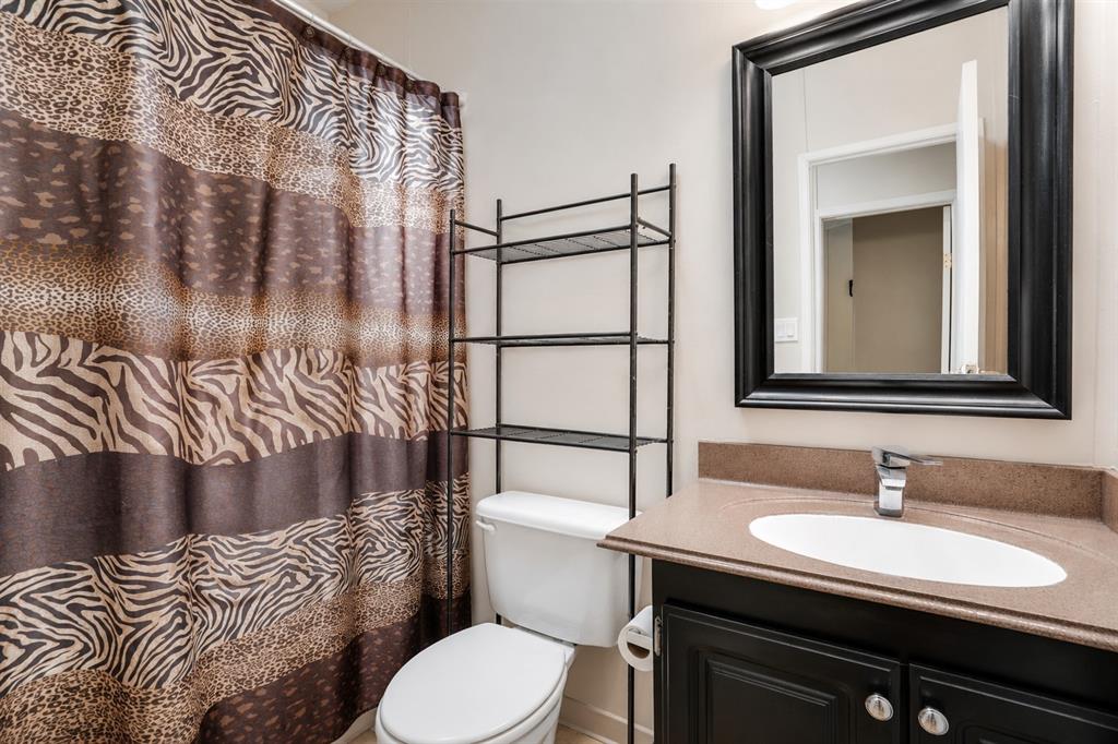 9455 Tranquil Acres Road Fort Worth, TX 76179 - Photo 8 of 20 Black framed mirror over a single vanity with a light brown countertop and dark cabinetry