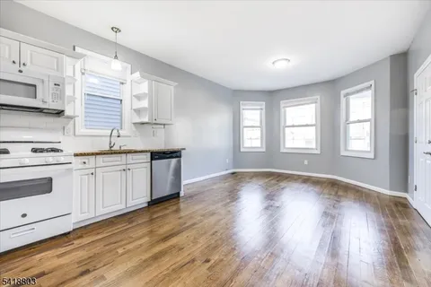 a kitchen with granite countertop a stove a sink and white cabinets with wooden floor