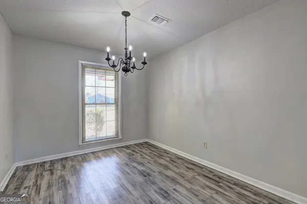 an empty room with wooden floor chandelier and windows