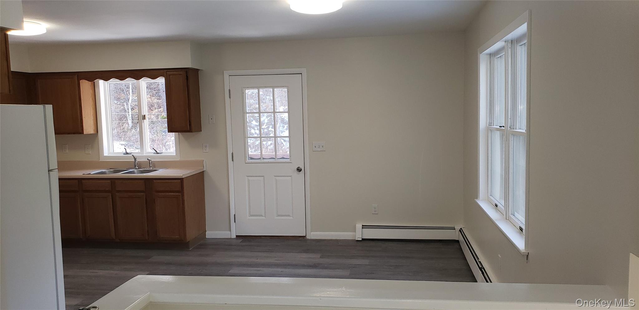 42 Upper Ferndale Road, Unit B Liberty, NY 12754 - Photo 3 of 18 Kitchen featuring freestanding refrigerator, light countertops, brown cabinetry, a baseboard radiator, and dark wood finished floors