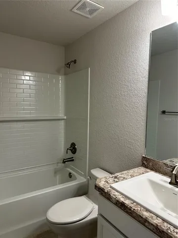 a bathroom with a granite countertop bathtub sink vanity mirror and toilet