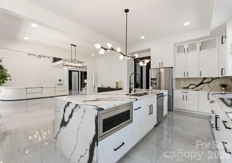 a large white kitchen with a large window a sink stainless steel appliances and cabinets
