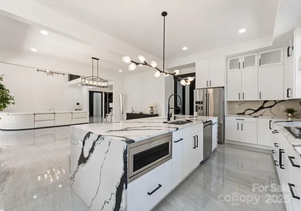 a large white kitchen with a large window a sink stainless steel appliances and cabinets