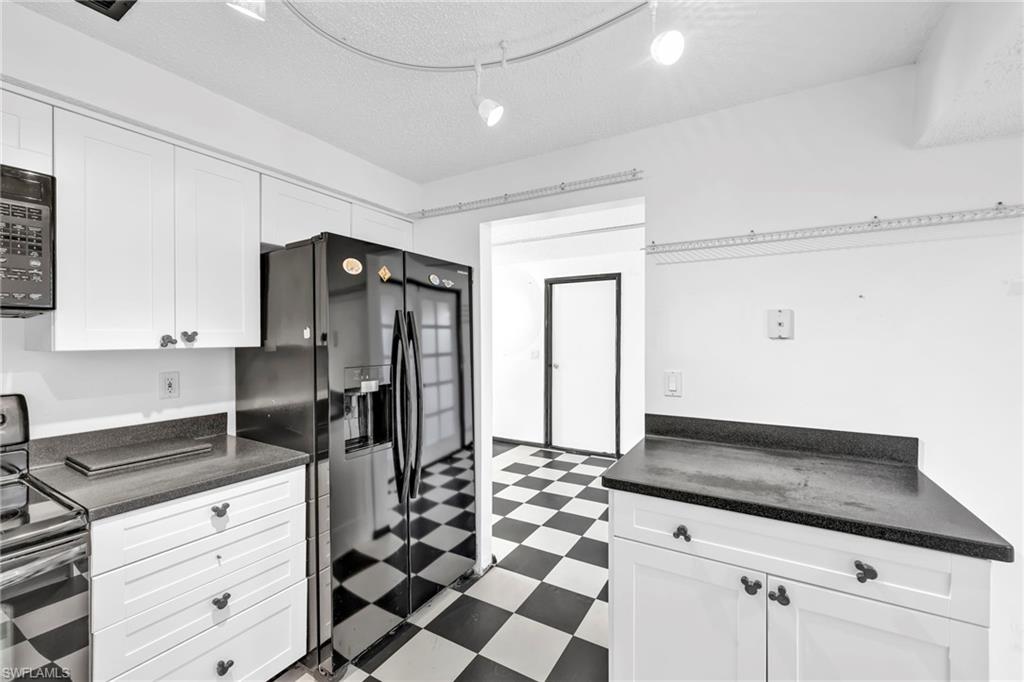 140 Blue Ridge Drive Naples, FL 34112 - Photo 11 of 26 Kitchen featuring tile patterned floors, black appliances, white cabinetry, dark countertops, and a textured ceiling